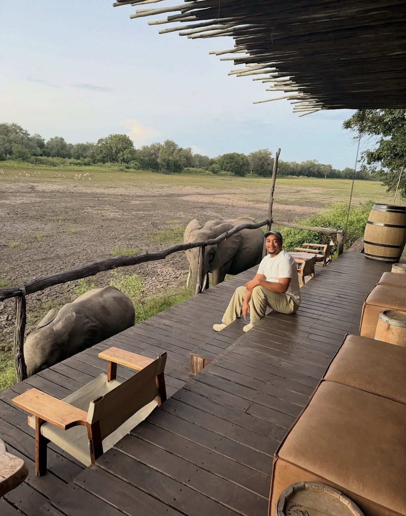 Zannon James seated on a lodge deck with elephants beside him