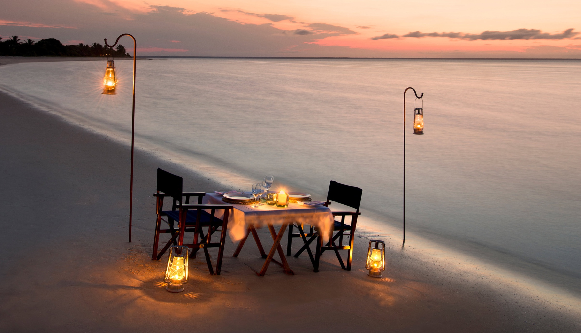 Lantern-lit dinner table on a Mozambique beach beside the Indian Ocean at dusk