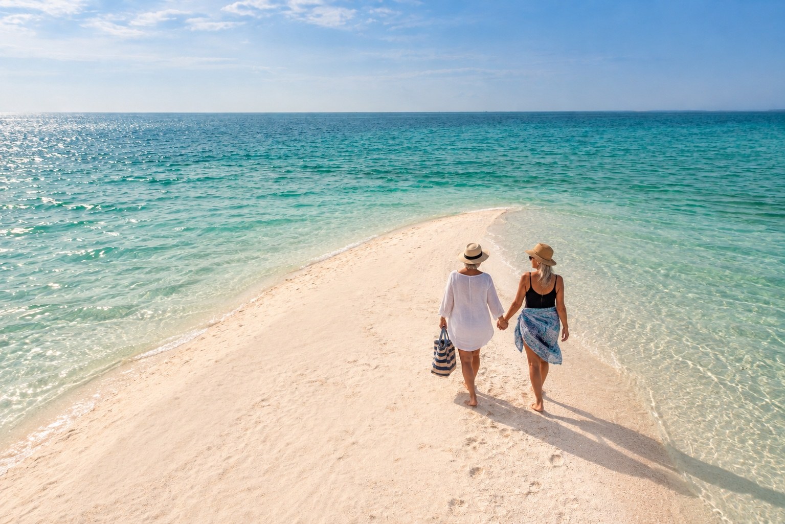 A same-sex couple walking hand in hand along a sandbank in Mozambique.