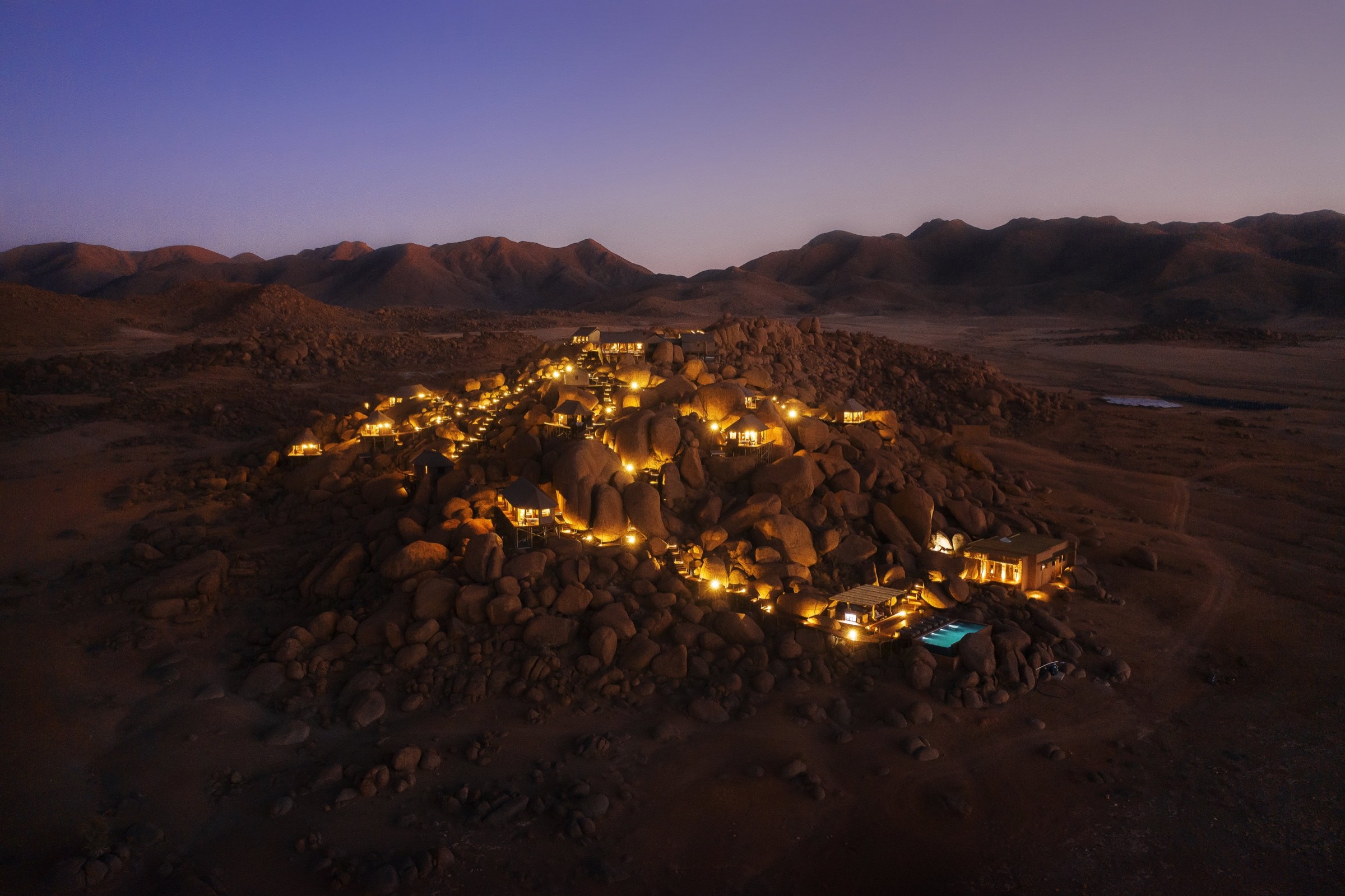 Illuminated desert lodge among rocky mountains in Namibia at dusk