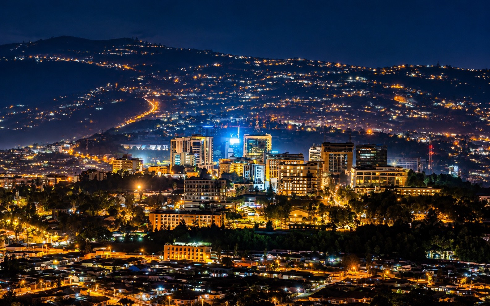 Kigali city buildings and hillside neighbourhoods lit up at night.