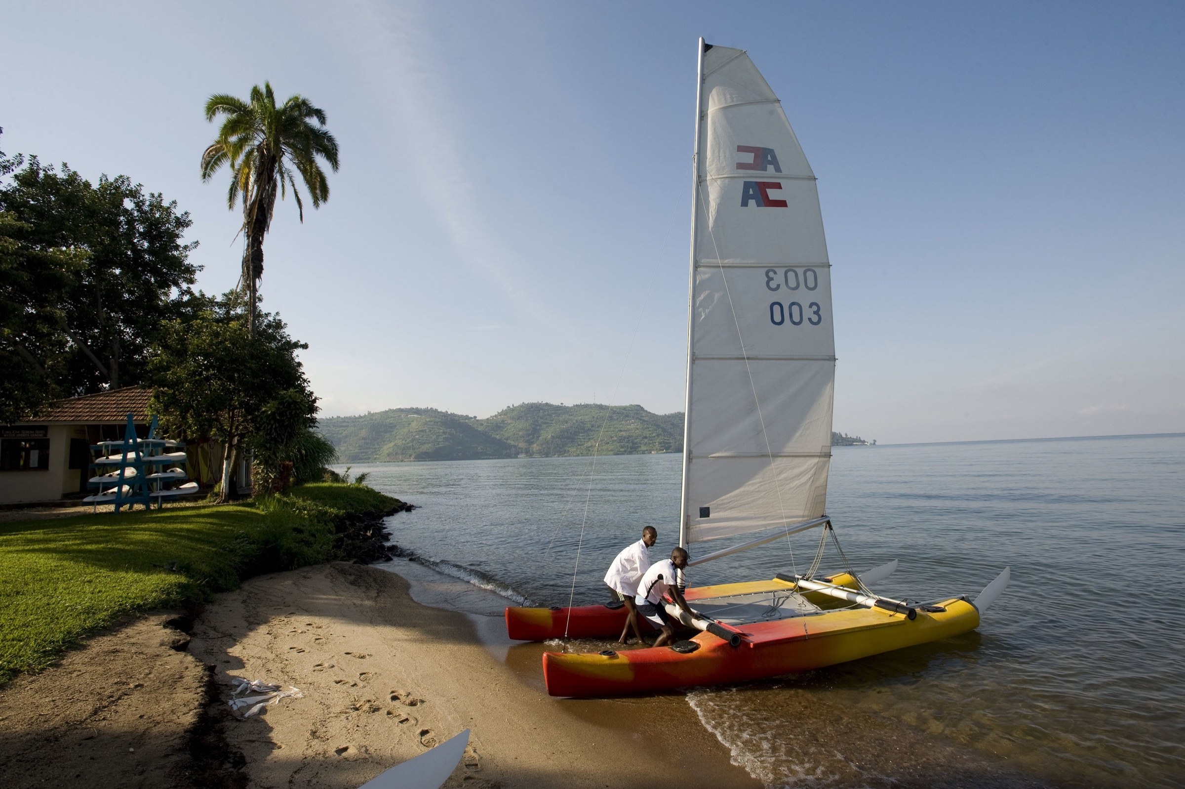 Two people preparing a sailing catamaran on the shore of Lake Kivu.