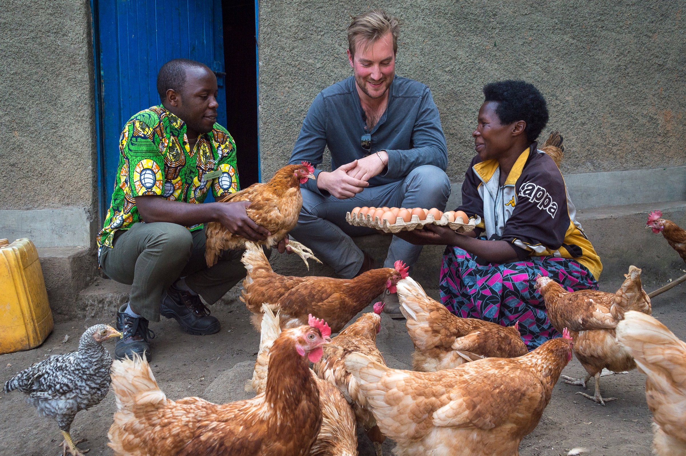 A visitor speaking with local hosts beside chickens and a tray of eggs in Rwanda.