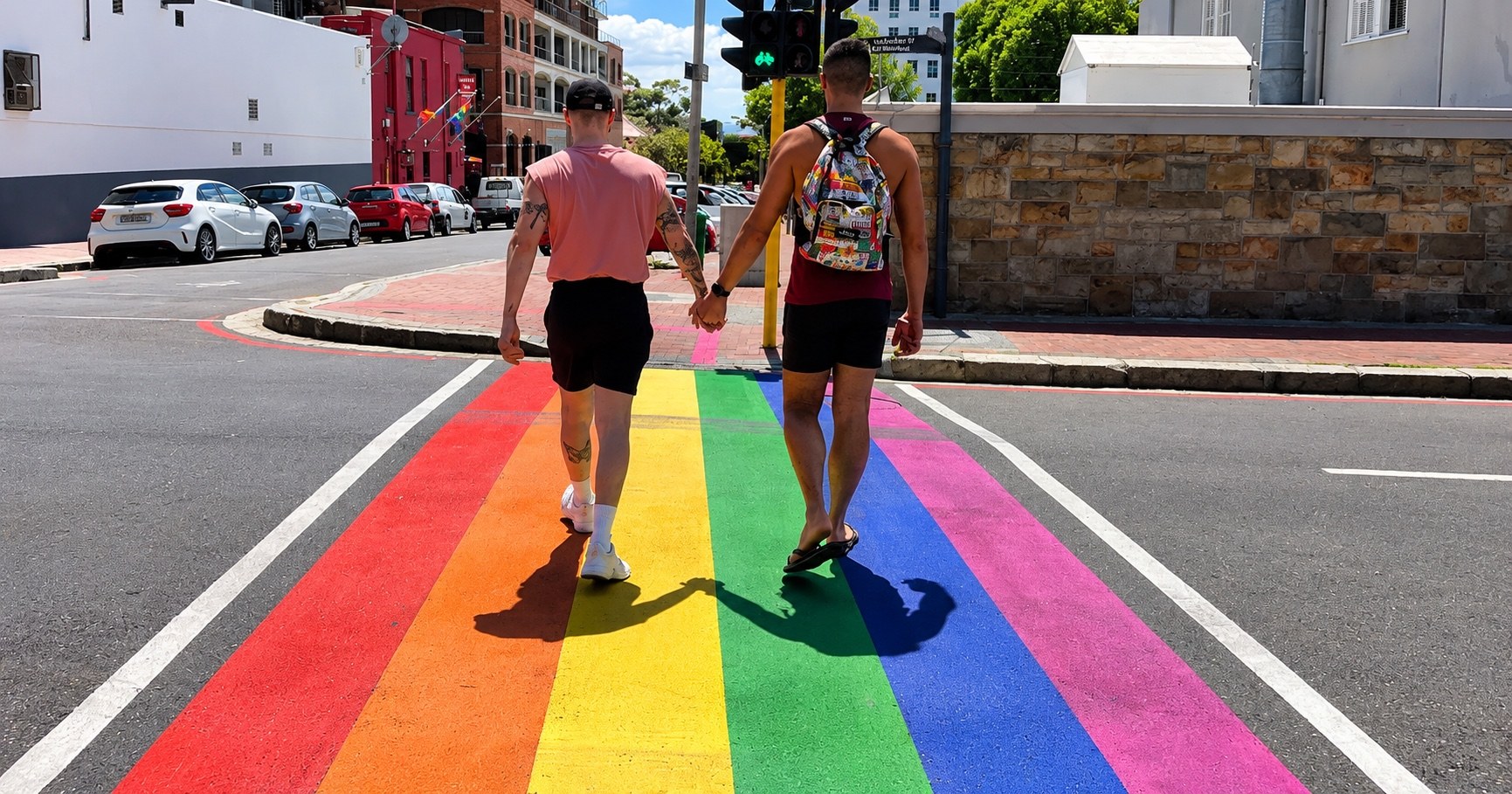 Two men walking hand in hand across a rainbow pedestrian crossing in Cape Town.