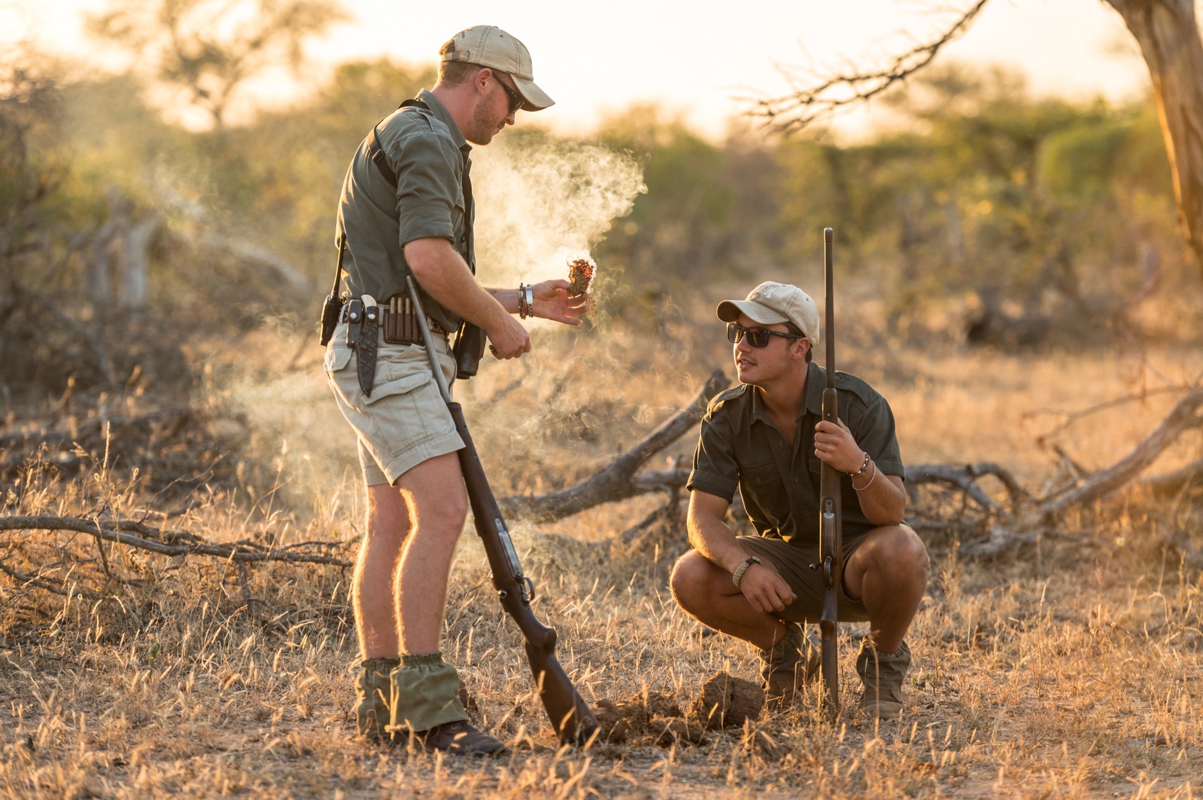 Two safari guides examining a smoking natural specimen in the bush.