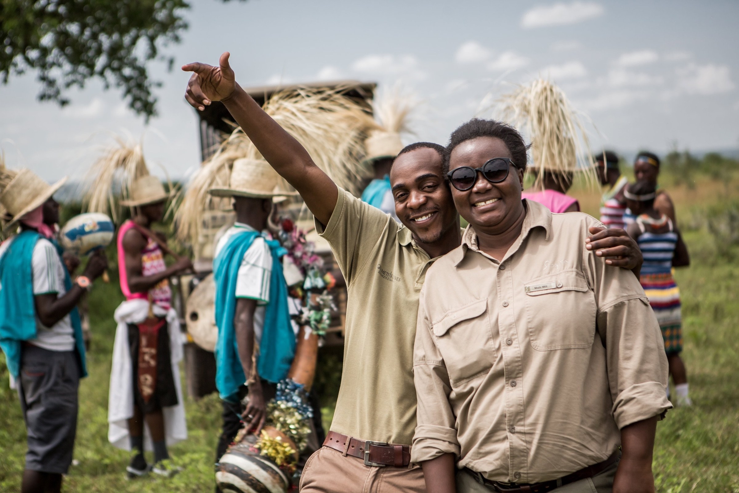 Two smiling members of a safari team together at a gathering with other people behind them.