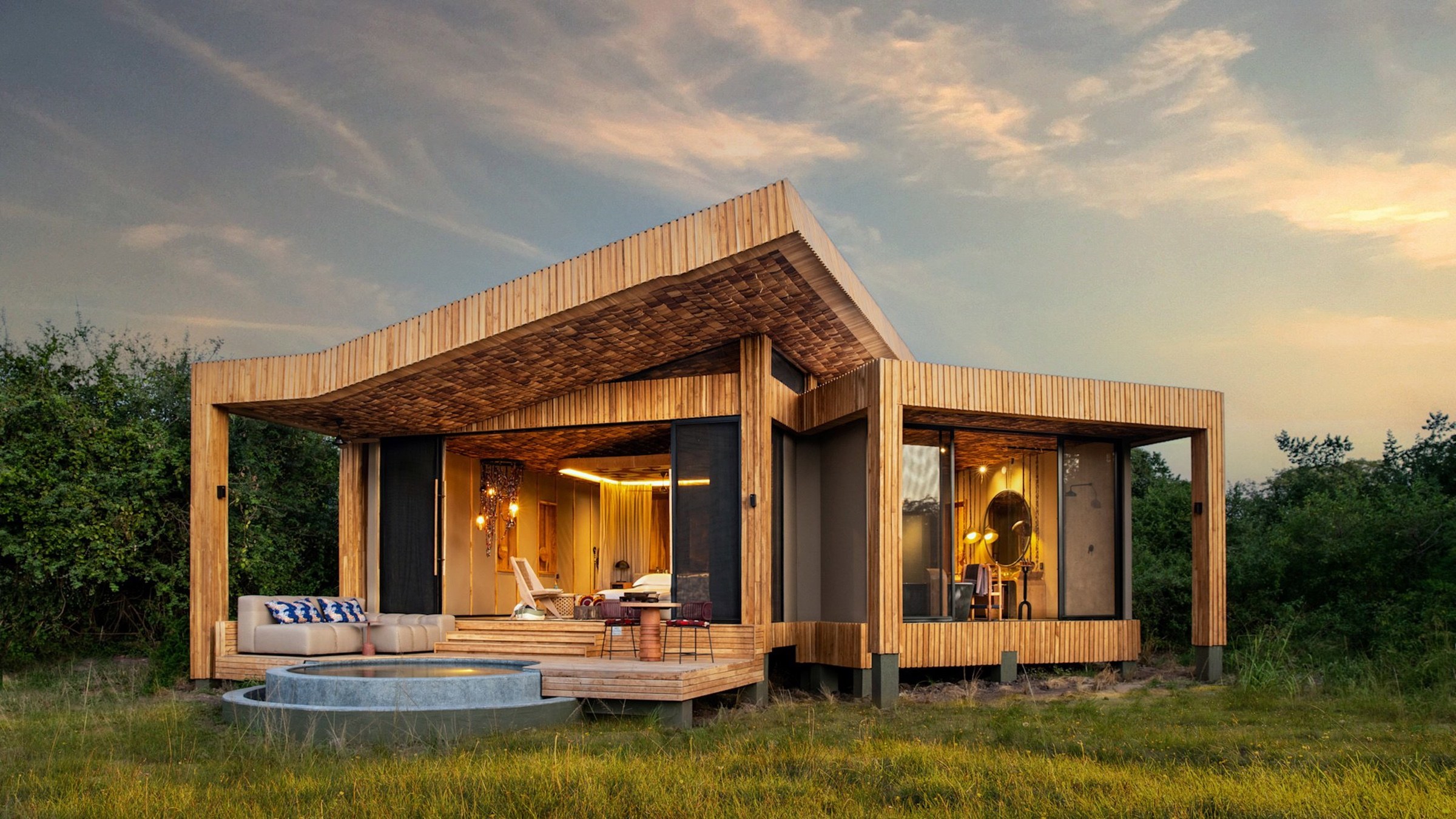 A timber safari villa with a private plunge pool and warm interior lighting at dusk.