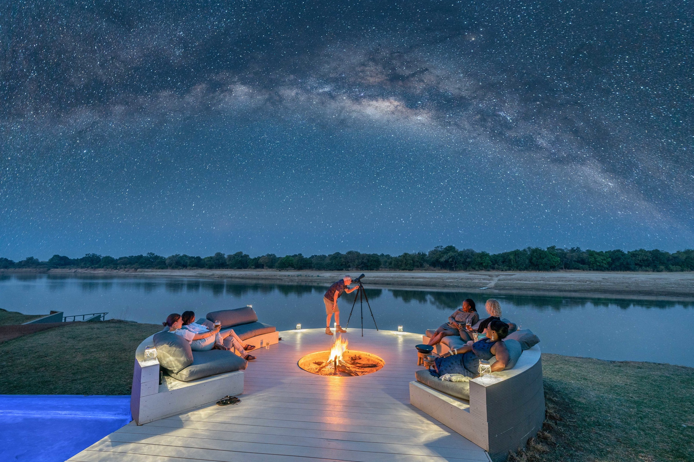 Guests beside a fire beneath the Milky Way in South Luangwa, Zambia