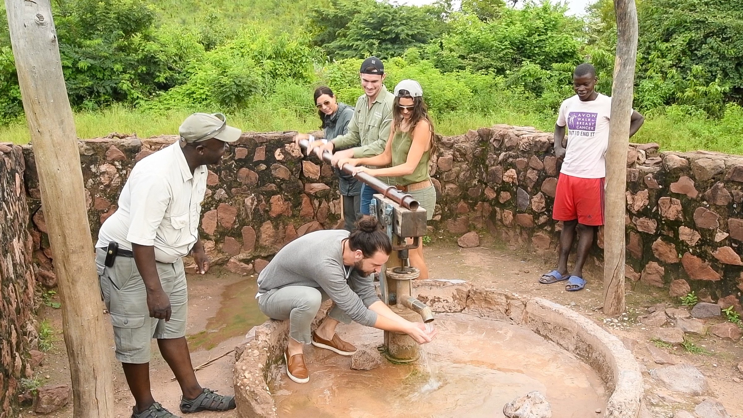 Visitors and local hosts using a hand-operated water pump in Zimbabwe
