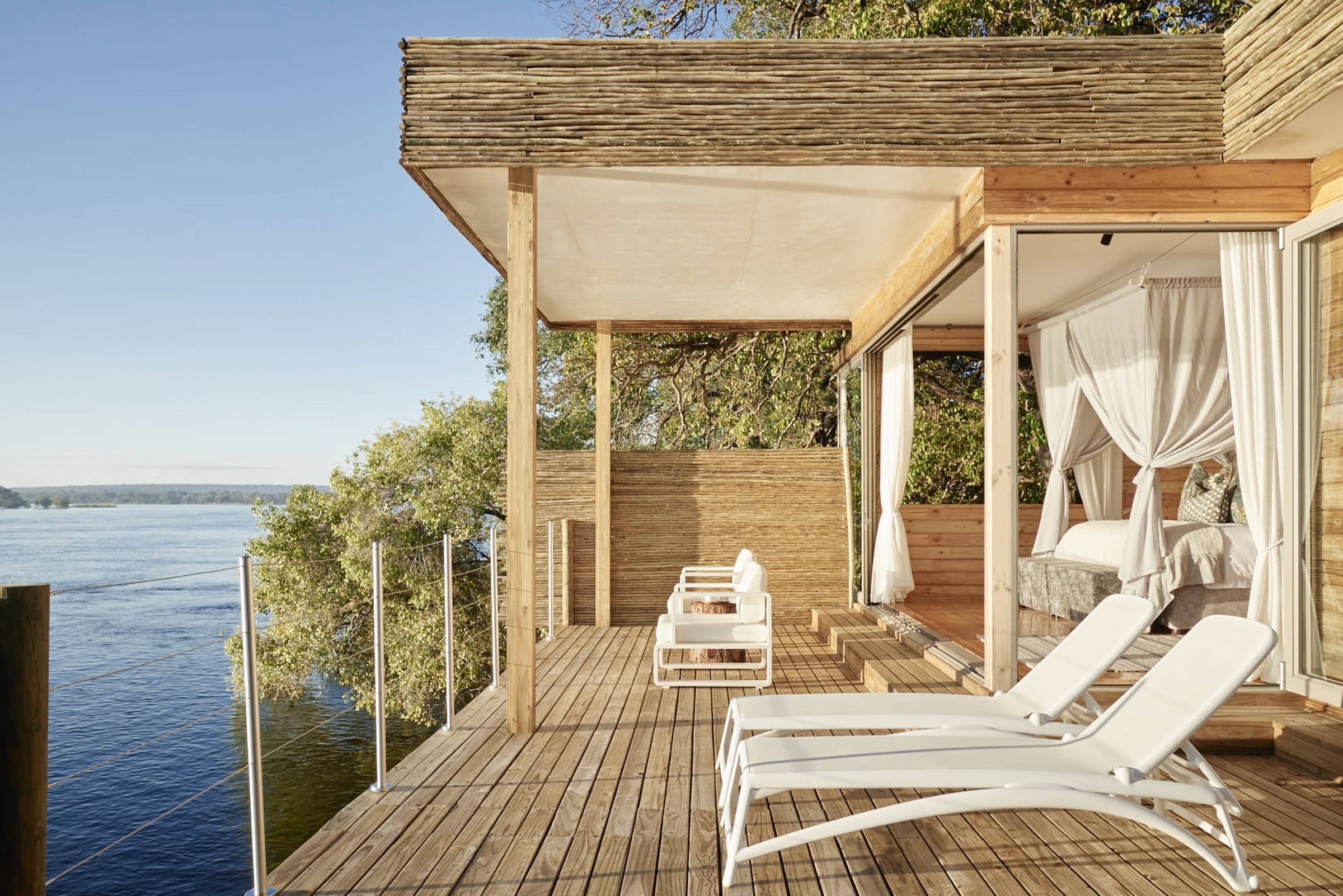 Wooden safari suite and deck with white loungers overlooking a river