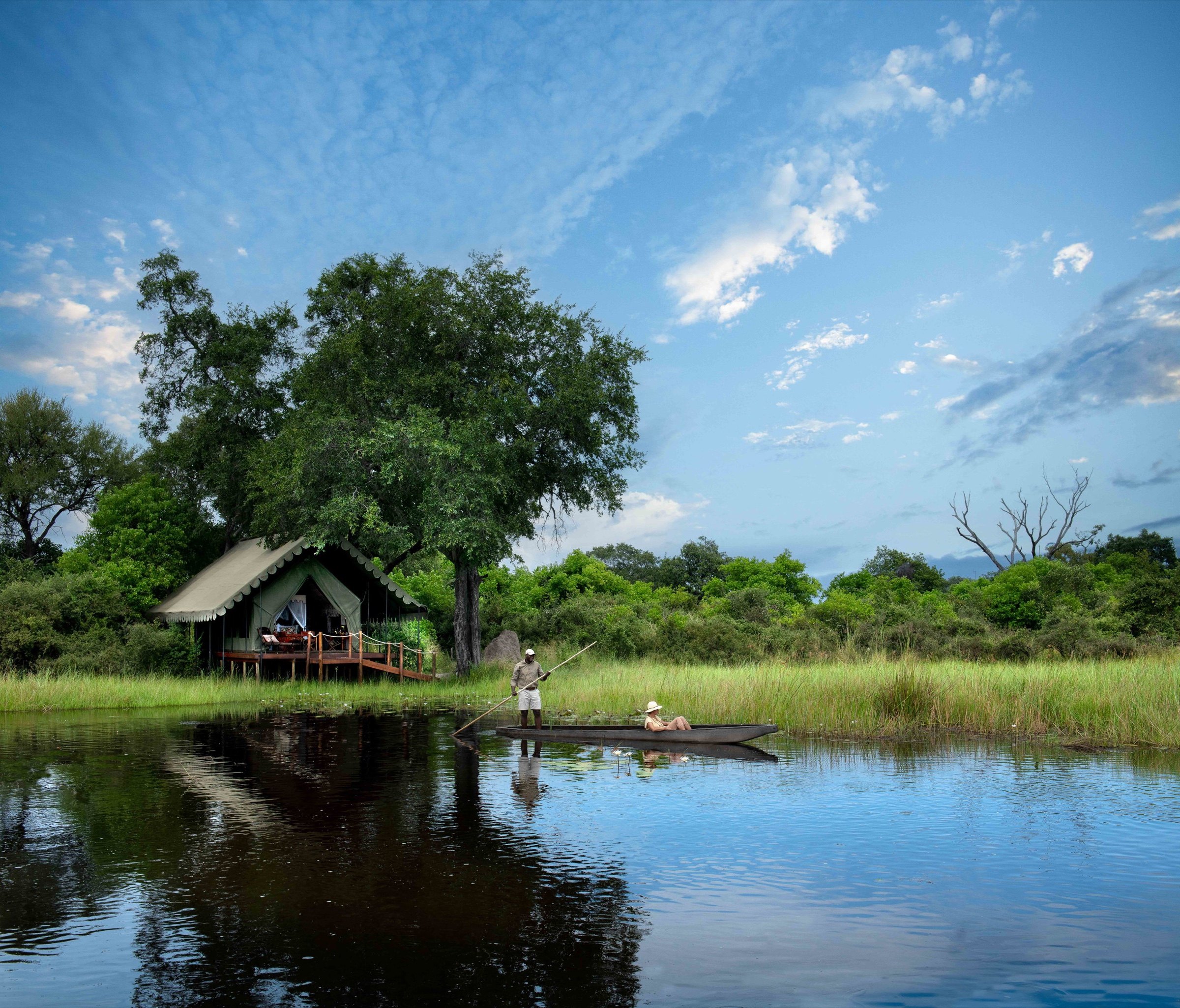 A guide poling a mokoro beside a tented camp in Botswana’s Okavango Delta