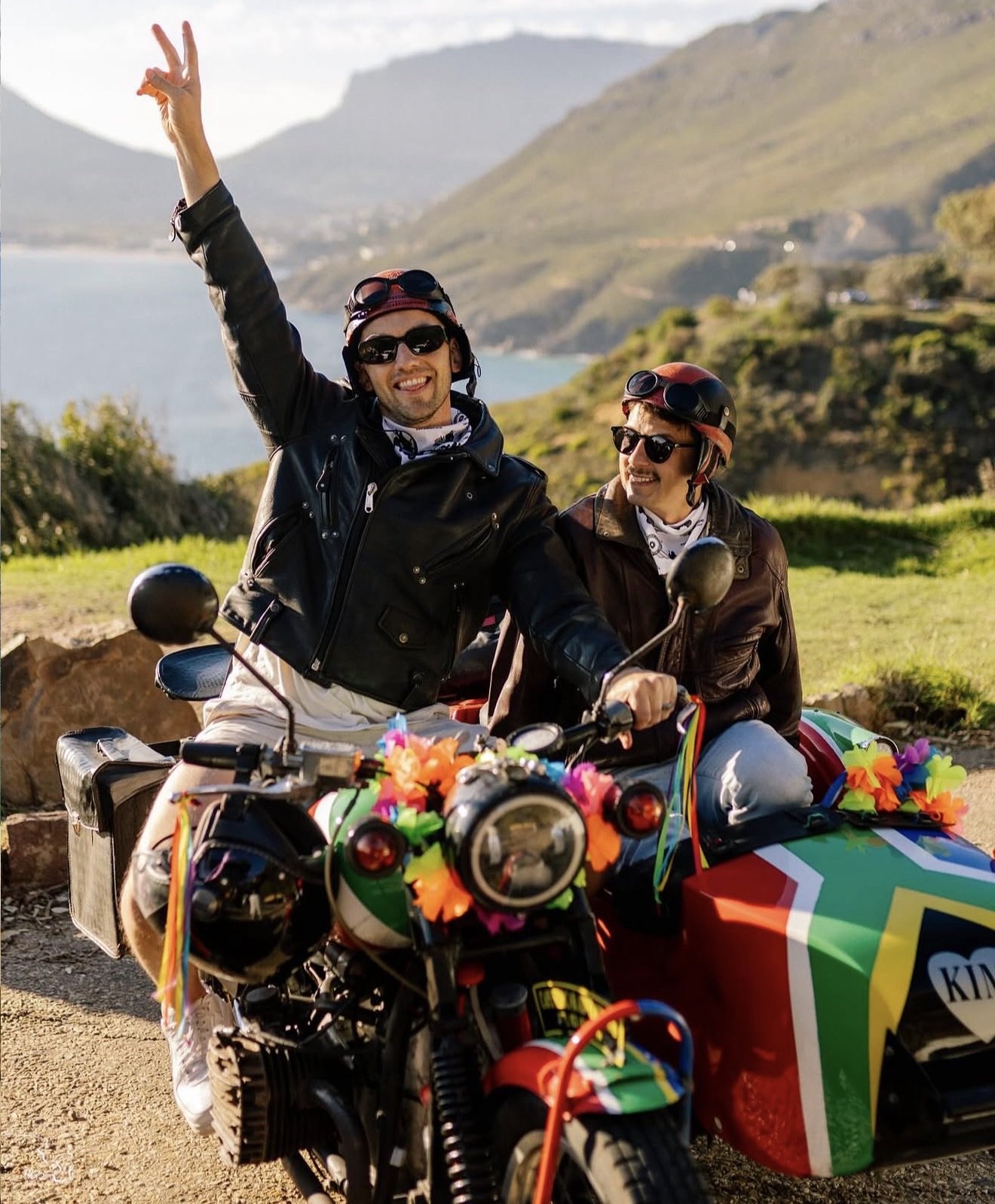 Two travellers on a decorated motorcycle and sidecar overlooking the Cape Town coast