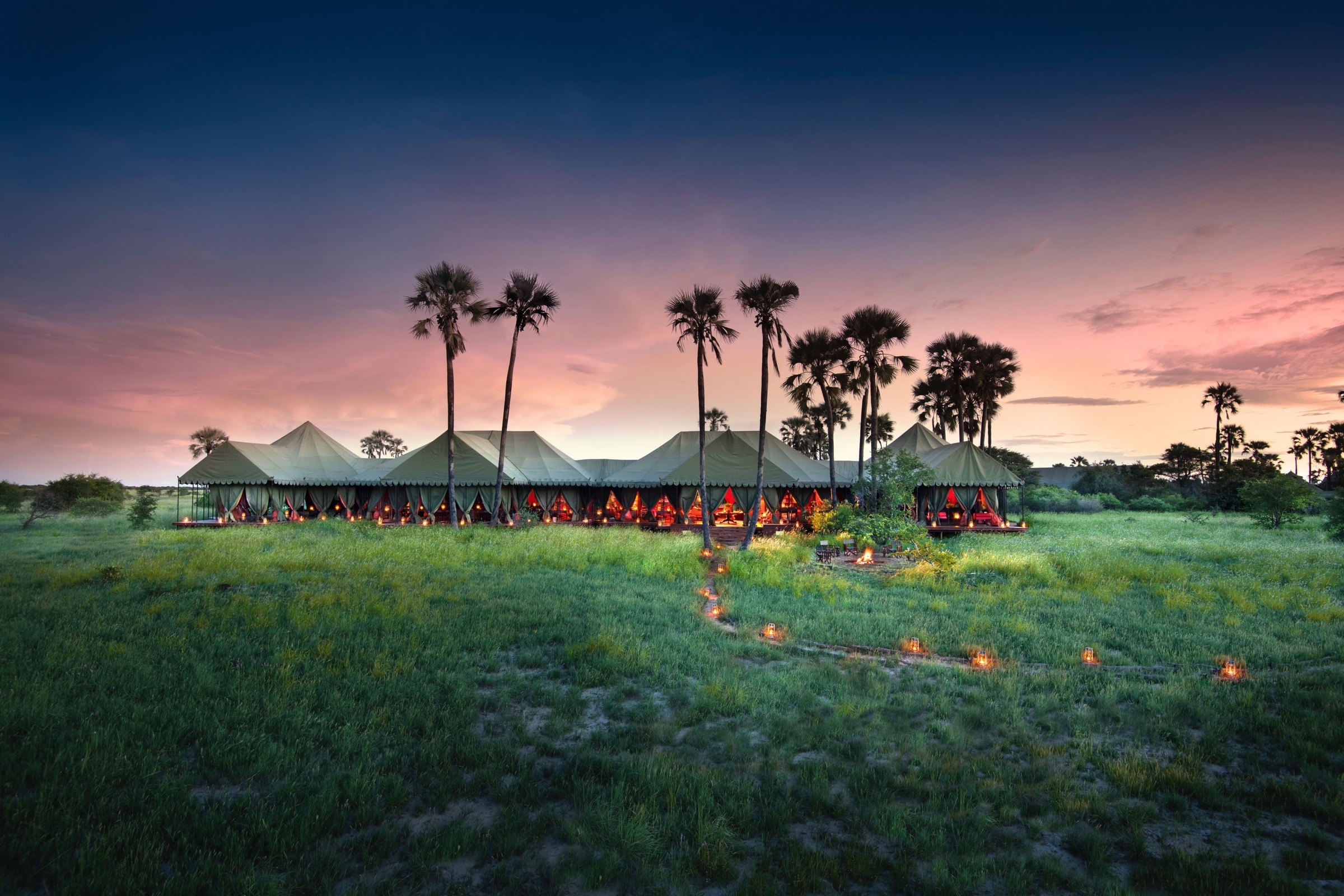 A remote tented safari camp among palms on Botswana’s Okavango floodplains at dusk